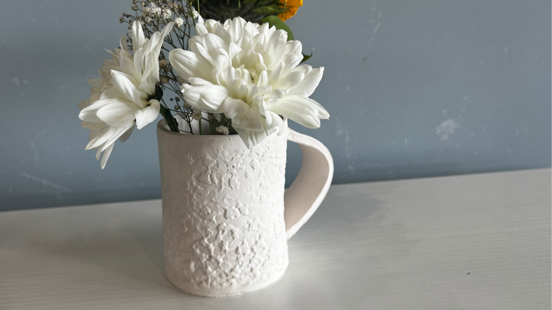 A pretty bisque fired pottery mug made during a pottery class at the Innovation Hub is filled with fresh flowers.