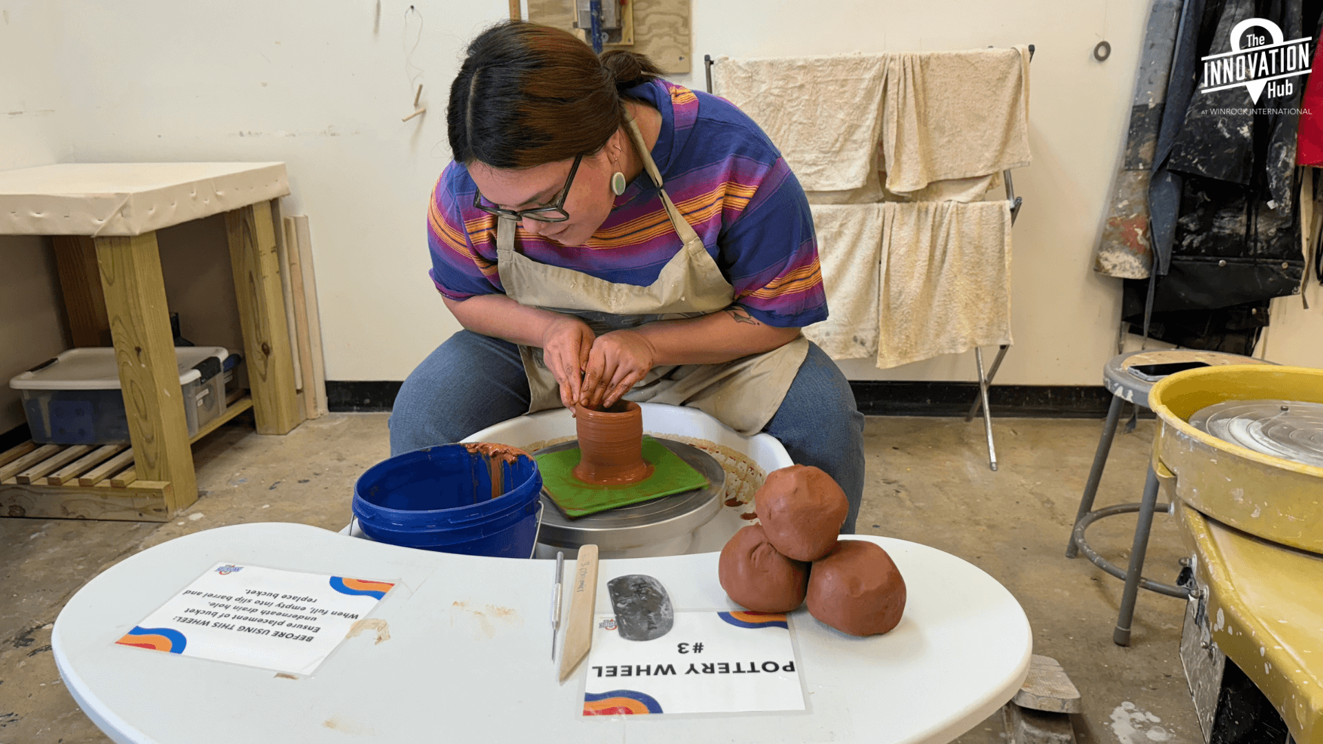A woman is on a pottery wheel, using red clay.