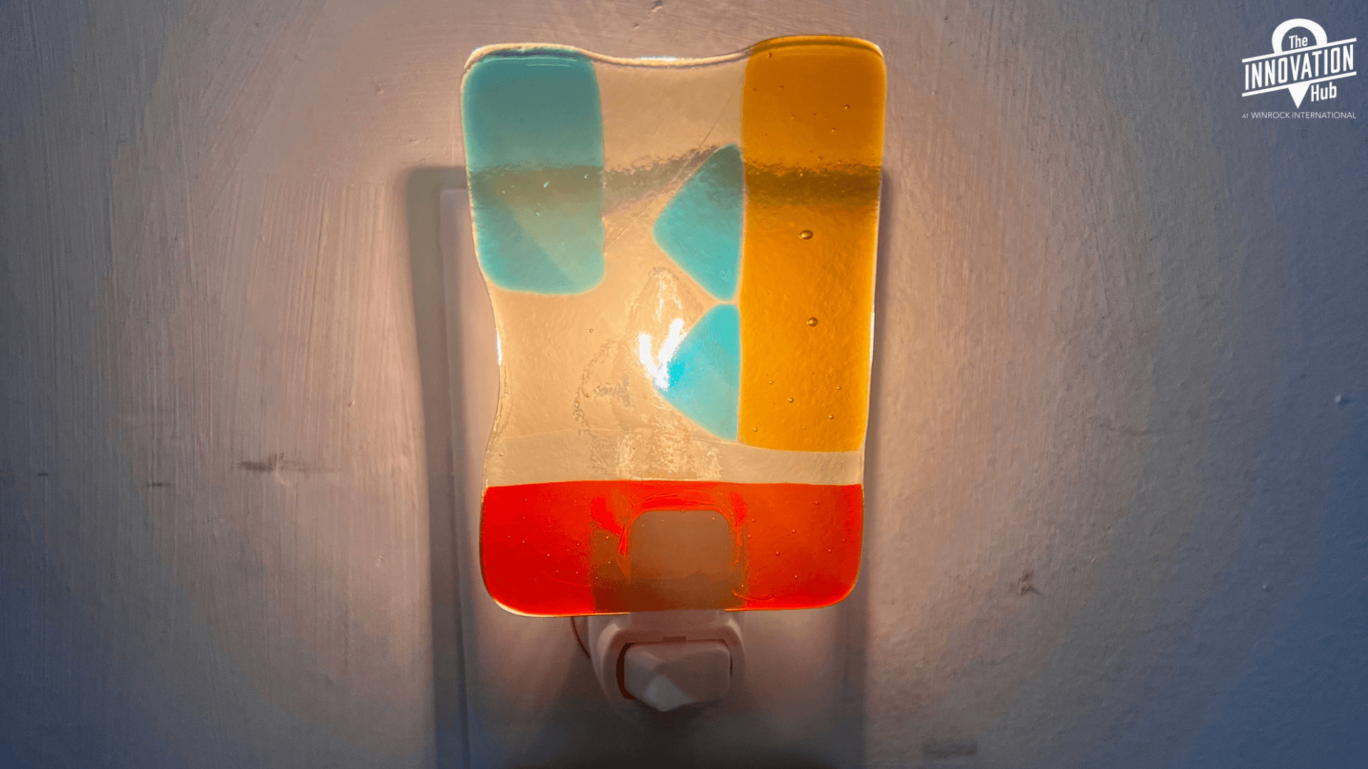 A color fused glass nightlight with teal, orange, red, and clear glass in a vertical rectangle shape. The night light is plugged in, so it illumiates beautifully.