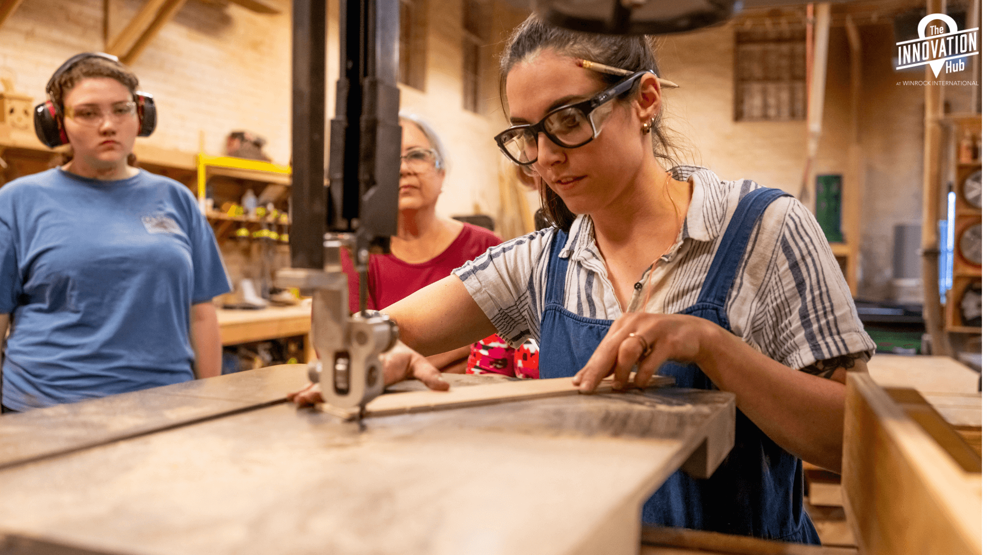 A woman using a bandsaw with others watching.