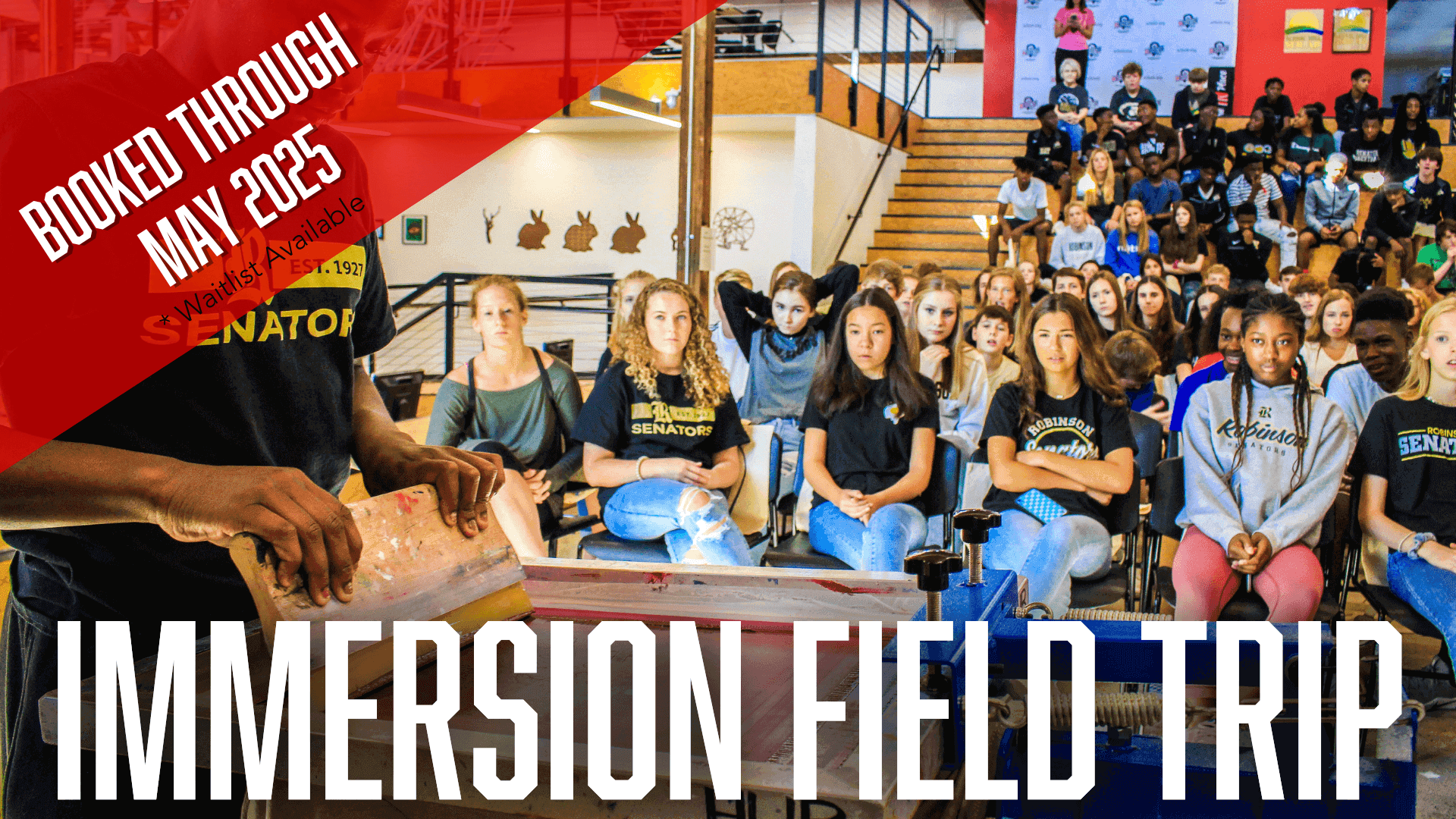 A group of students sit on bleachers and watch a screen printing demonstration before they attempt their own.